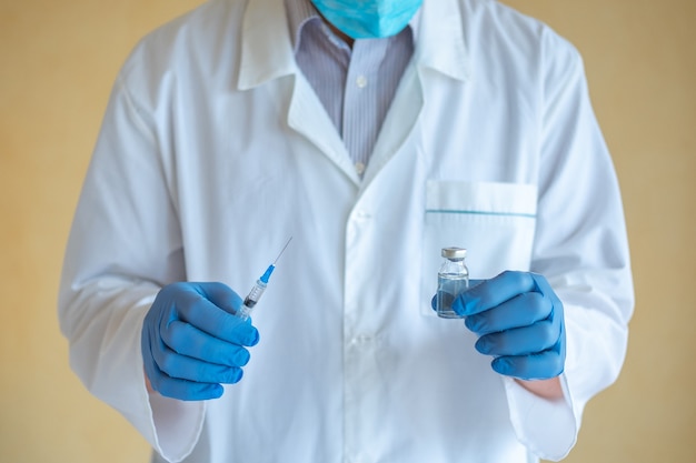 Foto médico homem com luvas de látex azul segurando uma seringa e uma ampola com vacina