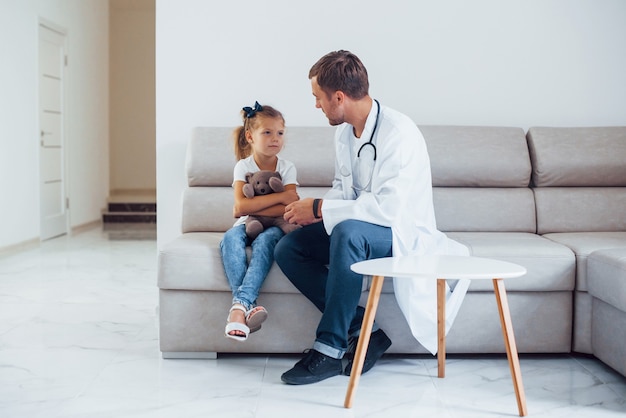 Médico homem de uniforme branco sentado na clínica com a menina.