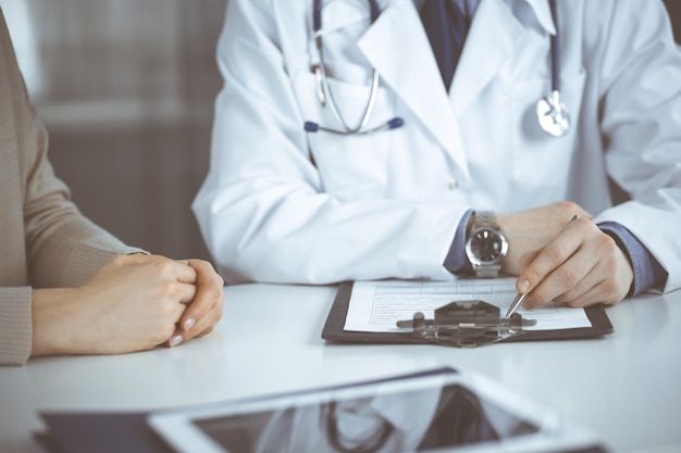 Médico homem desconhecido e paciente mulher discutindo algo enquanto sentado na clínica e usando clipboard. Melhor serviço médico no hospital, medicina, parada de pandemia.