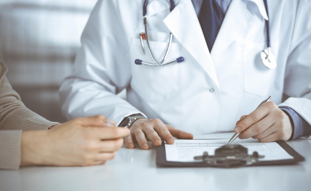 Médico homem desconhecido e paciente mulher discutindo algo enquanto sentado na clínica e usando clipboard. Melhor serviço médico no hospital, medicina, parada de pandemia.