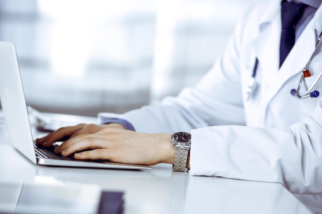 Médico homem desconhecido sentado e trabalhando com laptop na clínica em seu local de trabalho, close-up. Jovem médico no trabalho. Serviço médico perfeito, conceito de medicina.