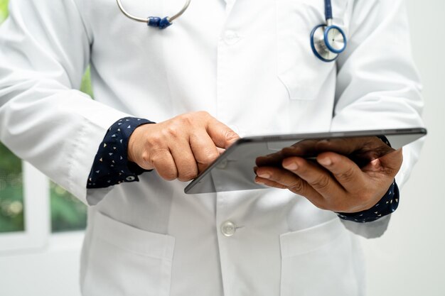 Foto médico homem inteligente asiático segurando tecnologia de tablet digital para pesquisar conhecimento resolver o tratamento para o paciente no hospital