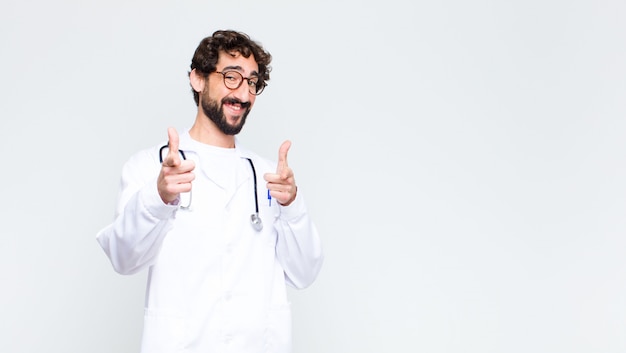 médico homem sorrindo com uma atitude positiva, bem sucedida e feliz apontando, fazendo sinal de arma com as mãos