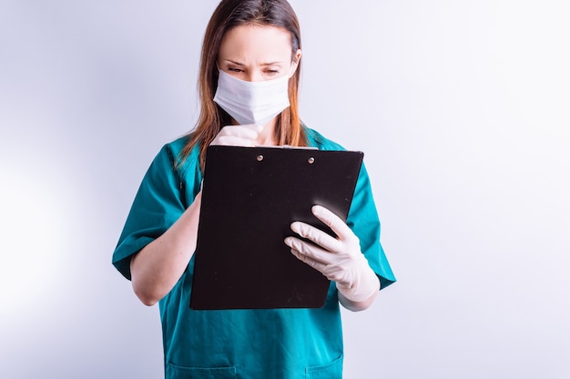 Médico del hospital con guantes de máscara sobre fondo blanco leyendo un informe completo de la medicina