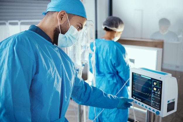 Médico hospital y máquina médica con pantalla de monitor durante la cirugía para la atención médica de diálisis y análisis en una habitación con mascarilla y exfoliantes Hombre cirujano presionando el botón en el dispositivo de cardiología