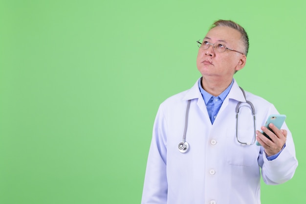 Médico japonés maduro con anteojos contra chroma key con pared verde