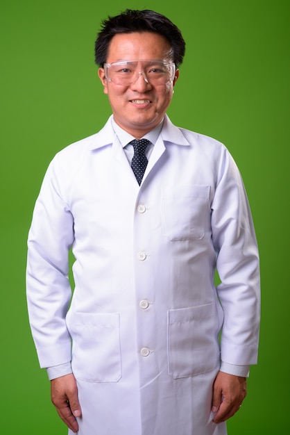 Médico japonês maduro usando óculos de proteção contra um fundo verde