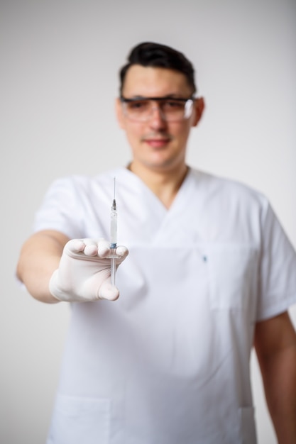 Médico jefe de sexo masculino en un traje quirúrgico blanco. Retrato de primer plano. Sostiene una jeringa con una inyección. Aislado sobre fondo blanco.