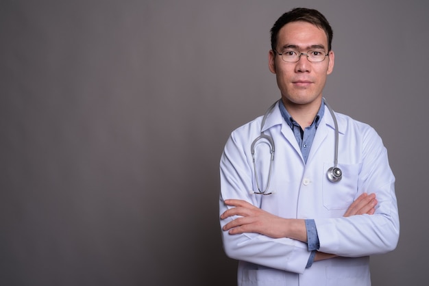 Médico jovem asiático contra uma parede cinza