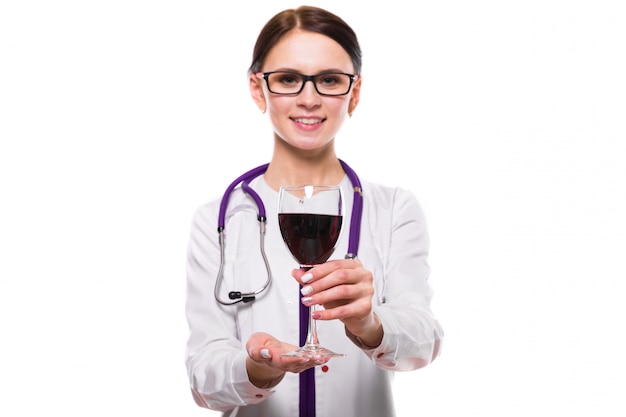 Médico jovem bonita com estetoscópio, oferecendo vinho em uniforme branco isolado