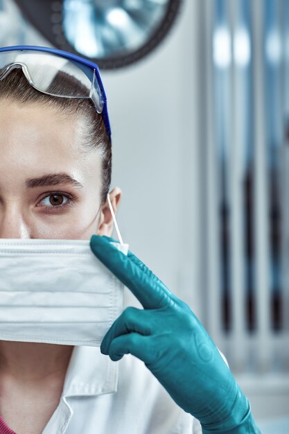 Médico jovem bonita de uniforme branco e máscara no rosto close-up no fundo da clínica