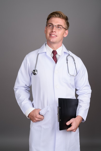 Médico jovem bonito, com cabelos loiros na parede cinza