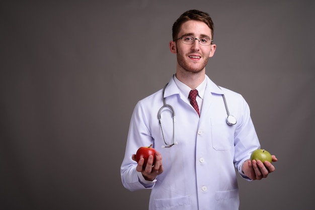 Médico jovem bonito usando óculos contra cinza