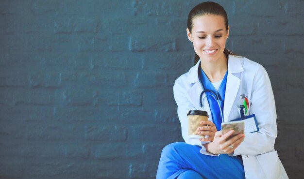 Médico jovem sentado com seu telefone Médicos de mulher