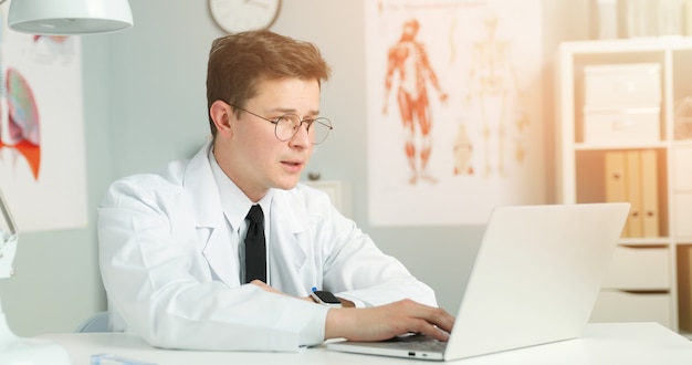 Médico jovem trabalhando com o laptop no gabinete de luz.