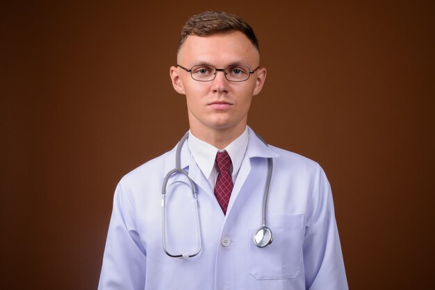 Médico jovem usando óculos em um fundo marrom