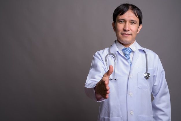 Médico joven asiático contra la pared gris