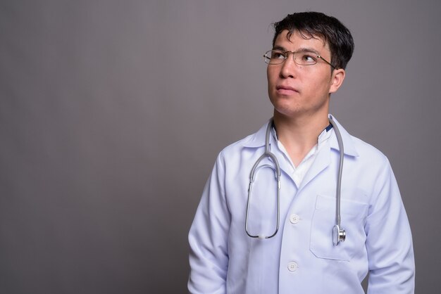 Médico joven asiático contra la pared gris