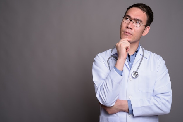 Médico joven asiático contra la pared gris