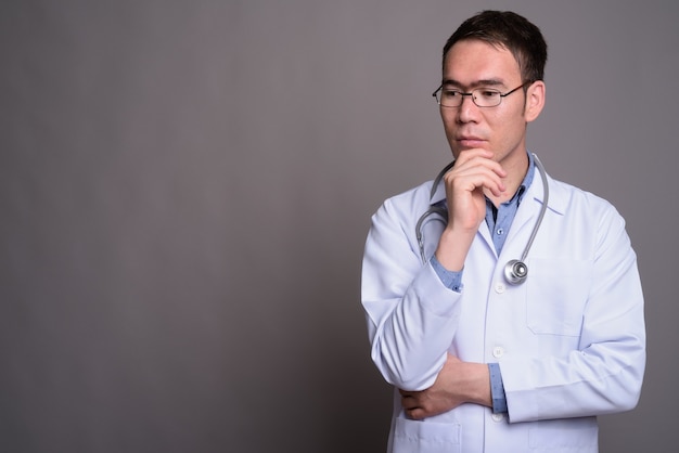 Médico joven asiático contra la pared gris