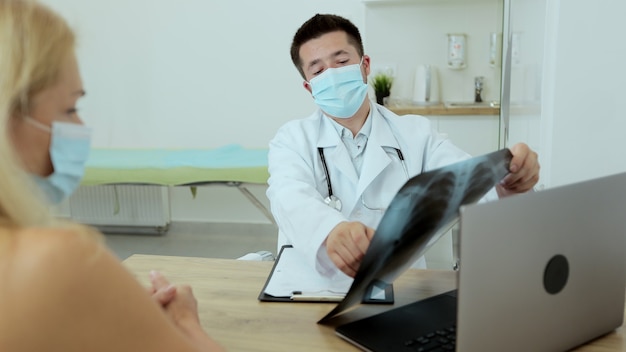 Médico joven con una bata blanca se comunica con los pacientes, retrato. El médico habla con un paciente, dice el diagnóstico, el pronóstico del tratamiento.