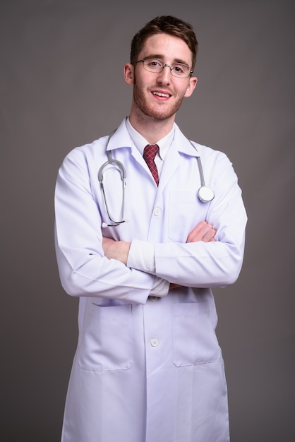 Médico joven guapo con anteojos contra gris