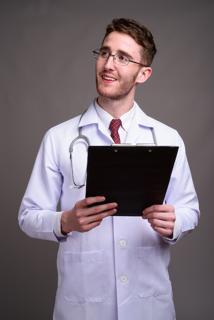 Médico joven guapo con anteojos contra gris