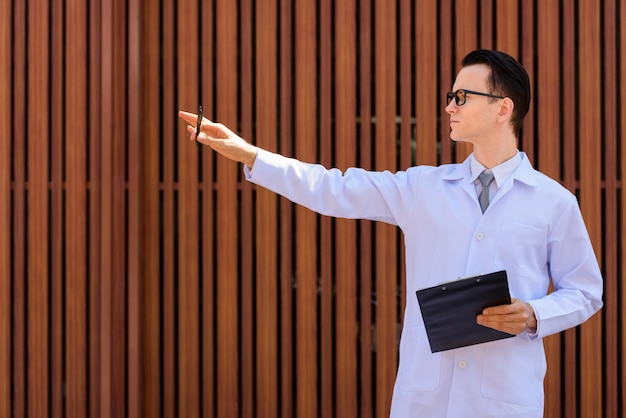 Médico joven guapo con anteojos sosteniendo portapapeles al aire libre