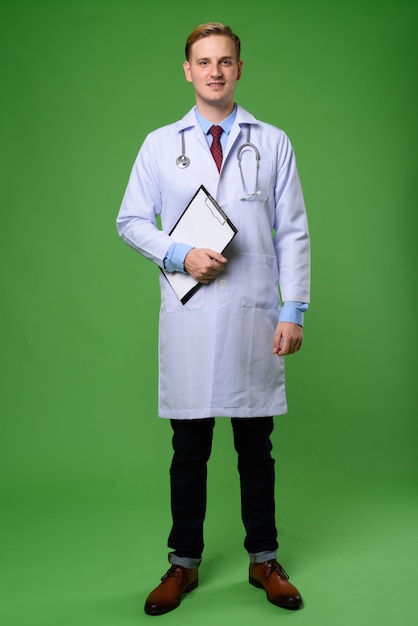 Médico joven guapo con cabello rubio contra backgrou verde