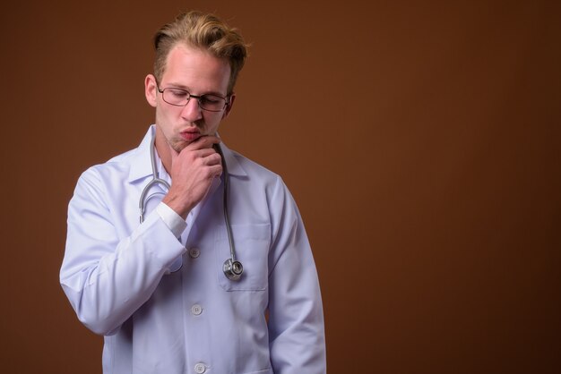 Médico joven guapo contra la superficie marrón