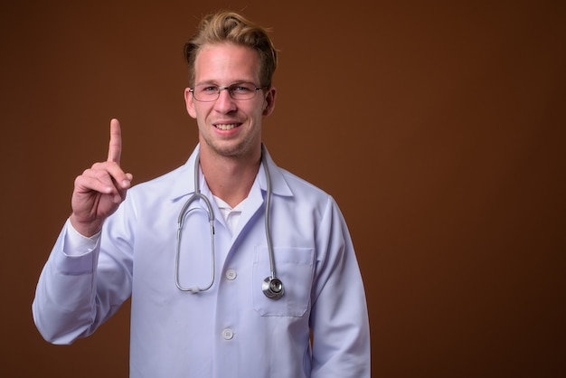 Médico joven guapo contra la superficie marrón