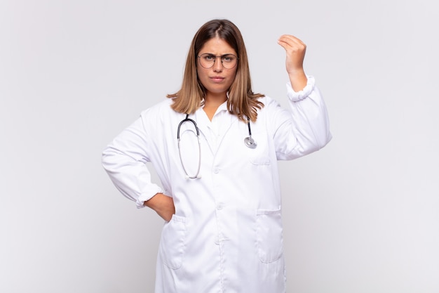 Médico joven haciendo capice o gesto de dinero, diciéndole que pague sus deudas!