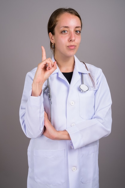 Médico joven hermosa contra el fondo gris