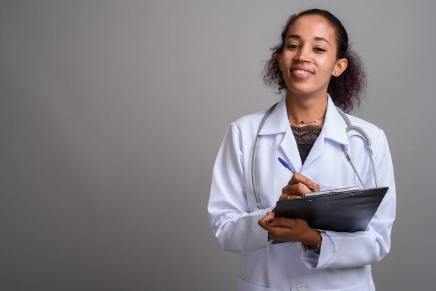 Médico joven hermosa mujer africana contra la pared gris