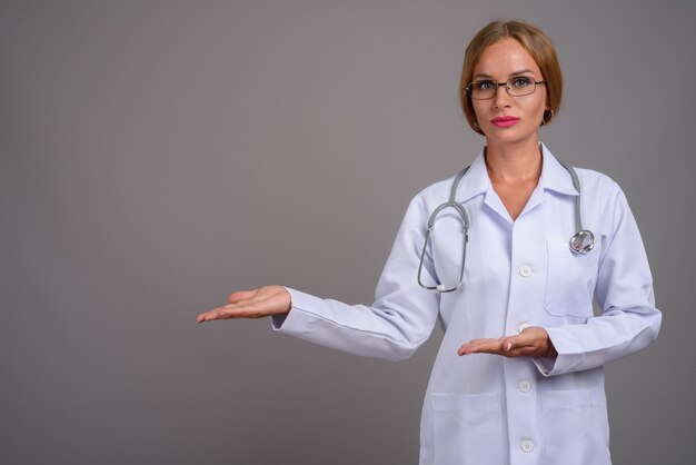 Médico joven hermosa con el pelo rubio contra backgr gris