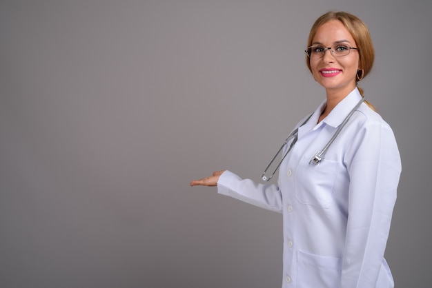 Médico joven hermosa con el pelo rubio contra backgr gris