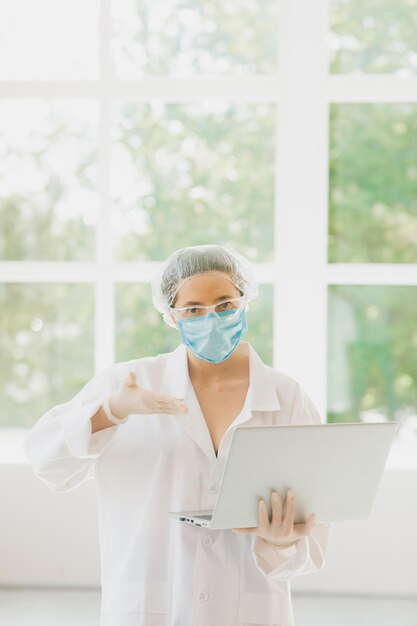 Médico en línea mujer con bata mascarilla guantes Sostenga la computadora portátil con la pantalla vacía