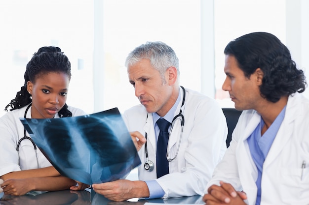 Médico maduro com dois colegas de trabalho trabalhando em um raio-x de pulmões