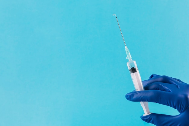 Foto médico mão usando luvas segurando a seringa no fundo azul