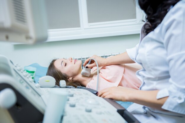 Médico con máquina de exploración de ultrasonido para examinar la tiroides de la mujer.