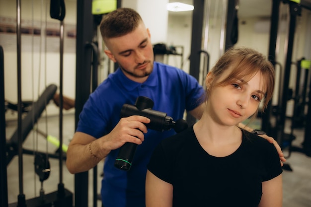 Foto un médico masajeando la espalda de una paciente con una pistola de masaje de percusión