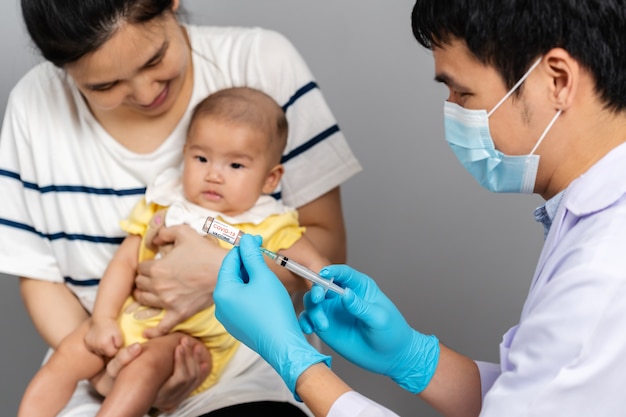 Un médico con una máscara extrae la vacuna contra el coronavirus (covid-19) del vial y la madre sostiene al bebé