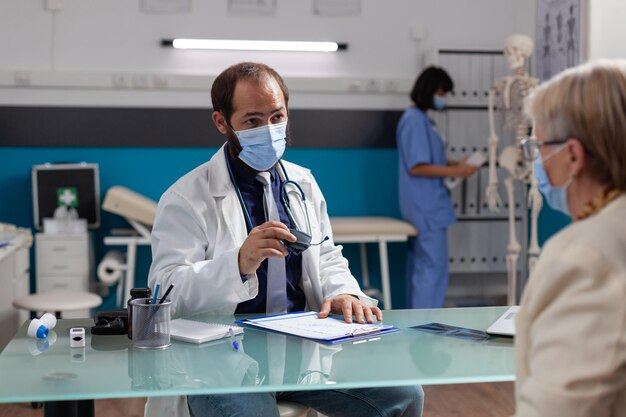 Foto médico con máscara hablando con un paciente en la clínica