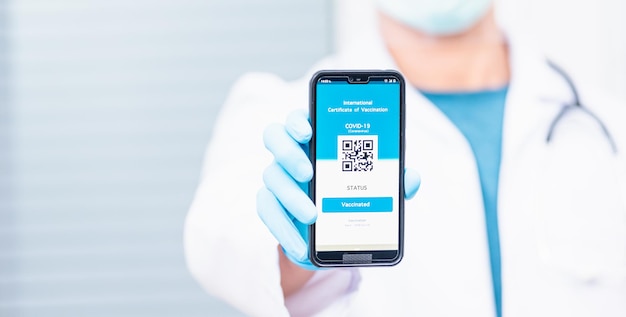 El médico en la máscara médica muestra la aplicación de teléfono inteligente pasaporte digital vacunado certificado de COVID-19.