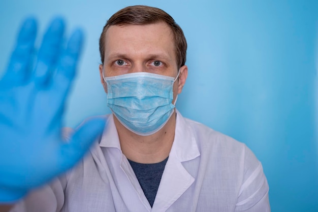 Un médico con una máscara médica muestra una parada con la mano en un fondo azul