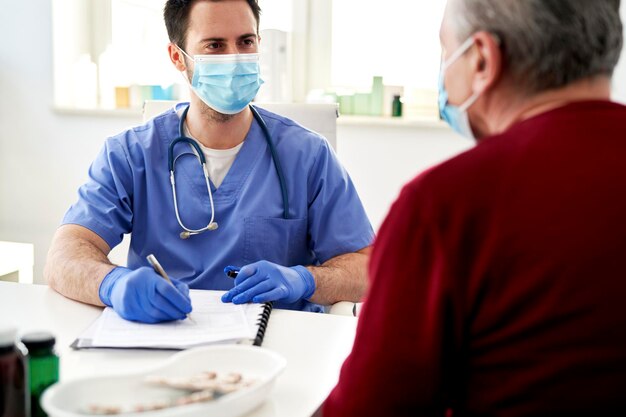 Médico con máscara protectora hablando con un paciente mayor