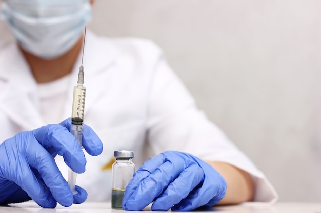 Un médico con mascarilla y guantes sosteniendo una botella de vacuna y una jeringa de cerca