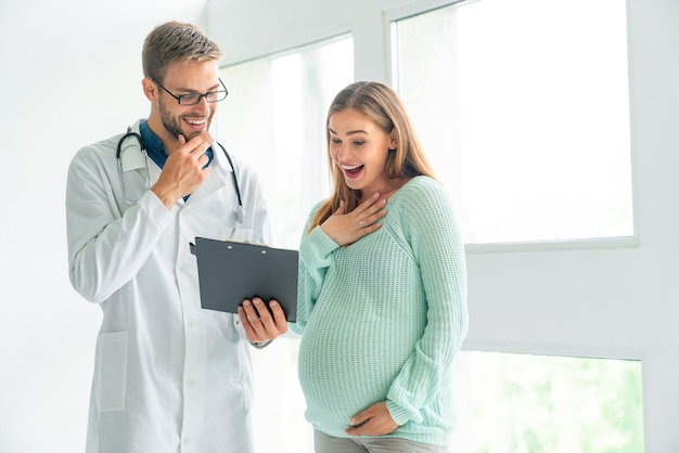 Médico masculino a mostrar um documento de receita a uma mulher grávida na clínica
