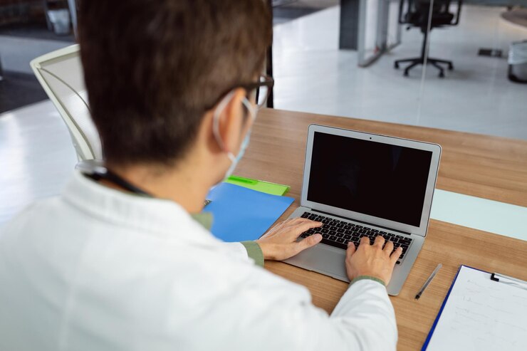 Foto médico masculino asiático con mascarilla sentado en el escritorio de la oficina del hospital usando una computadora portátil. servicios médicos y sanitarios durante la pandemia del coronavirus covid 19.