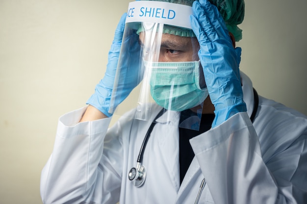 Médico masculino asiático usando escudo facial e uniforme com estetoscópio